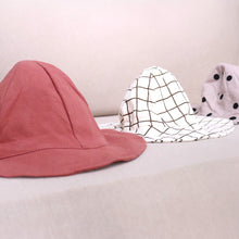 Load image into Gallery viewer, Three baby cotton bucket hats. Brown and white grid pattern, solid red, and beige with black polka dots.