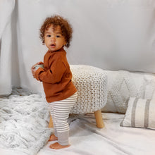 Load image into Gallery viewer, A toddler standing wearing a brown long sleeved mock-neck shirt with scalloped hems and light grey and white striped cotton baby leggings with a light grey ribbed cuff at the bottom.