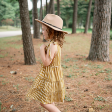 Load image into Gallery viewer, toddler standing facing her right wearing brown hat and gold gingham tiered toddler dress with hand tied bow straps