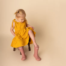 Load image into Gallery viewer, child sitting putting on pink rainboots wearing yellow gold strapless tiered dress