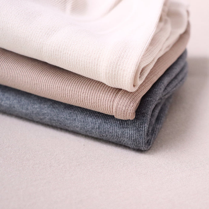 Baby pants folded on top of each other: cream, camel and charcoal