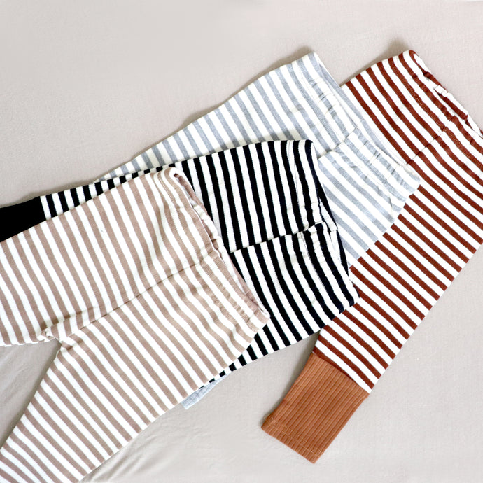 Four pairs of striped cotton baby leggings in the colors tan, black, light grey and brown.