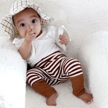 Load image into Gallery viewer, Baby sitting wearing white and brown grid cotton baby bucket hat wearing a white flutter sleeve shirt and white and brown striped leggings
