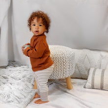 Load image into Gallery viewer, A toddler standing wearing a brown long sleeved mock-neck shirt with scalloped hems and light grey and white striped cotton baby leggings with a light grey ribbed cuff at the bottom.
