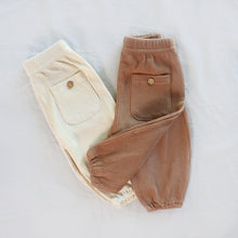 Load image into Gallery viewer, Baby cream waffle pants folded vertically laying next to brown waffle pants both showing back pocket with button
