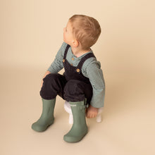 Load image into Gallery viewer, Toddler sitting looking to the right wearing dark denim jumpsuit, green striped long sleeved shirt and green rain boots
