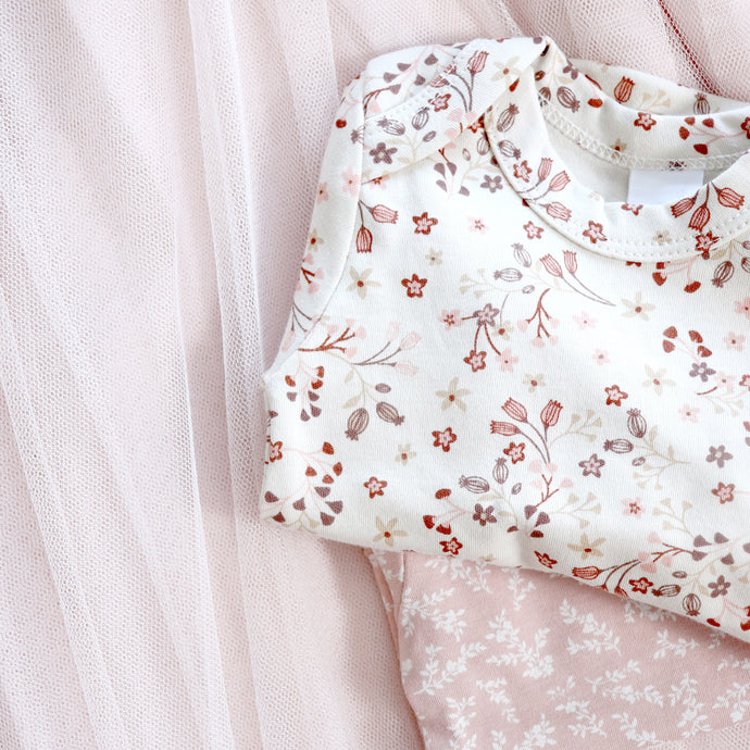 white baby onesie with pink floral design folded on top of pink baby onesie with white floral design