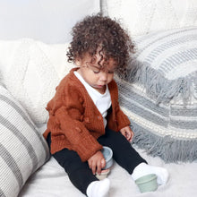 Load image into Gallery viewer, Baby sitting playing wearing a white long sleeve shirt and brown knit pom pom cardigan with black leggings
