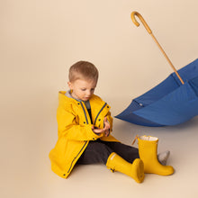 Load image into Gallery viewer, toddler sitting holding blue umbrella wearing yellow rain jacket and yellow rain boots 
