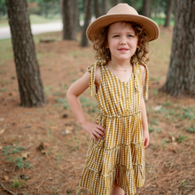 Load image into Gallery viewer, child standing with hand on hip next to trees wearing brown hat and gold gingham tiered toddler dress with hand tied bow straps

