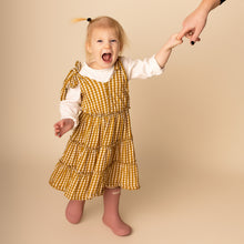 Load image into Gallery viewer, toddler standing smiling wearing white long sleeved shirt, yellow gold gingham strapless tiered dress and pink rainboots
