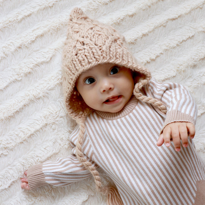 baby laying on white blanket wearing latte colored knit bonnet and white and tan striped onesie