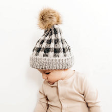 Load image into Gallery viewer, Baby wearing grey buffalo checkered knit hat with ribbed cuff and fur pom pom topper and beige knit top

