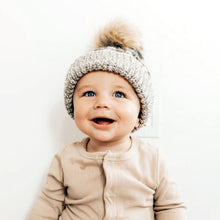Load image into Gallery viewer, Baby smiling wearing grey buffalo checkered knit hat with ribbed cuff and fur pom pom topper and beige knit top
